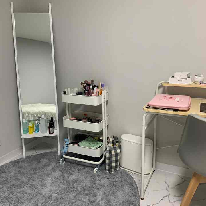 A simple modern small room in white and gray tones featuring a full-length mirror, desk, chair, and storage shelf neatly arranged.
