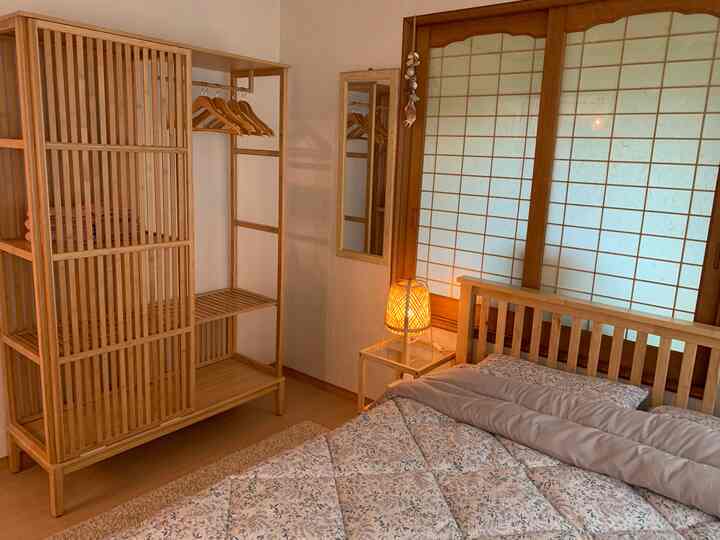 明るいナチュラルカラーの小さな寝室、木製のクローゼットとベッド、暖かい照明が印象的なゲストルーム