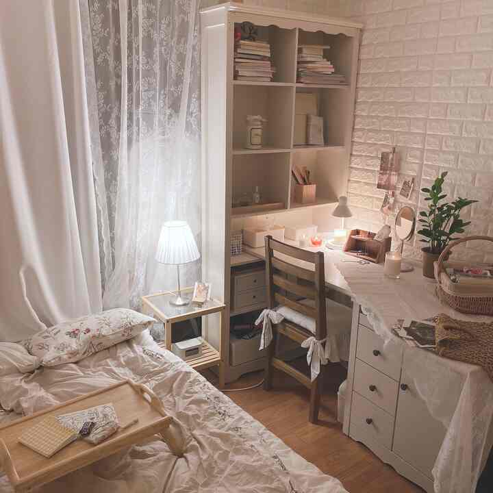 Cozy bedroom with white and natural wood tones featuring a wooden desk, bed, lace curtains, and candles