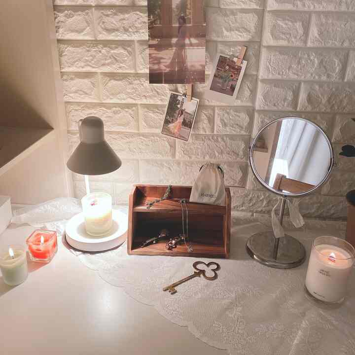 白いレンガ壁とレースカーテンを背景にしたデスク上に、キャンドルや鏡、木製小物が配置された居心地の良いホームオフィス空間