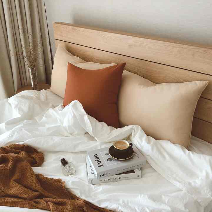 Beige and white toned bedroom featuring a wood headboard, cushions, and a coffee cup creating a cozy atmosphere