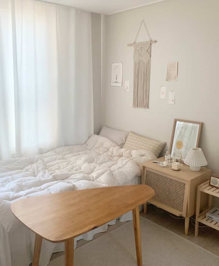 Beige-walled bedroom with white bedding, featuring a wooden coffee table and nightstand creating a warm natural atmosphere