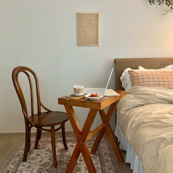 Soft beige and light brown bedroom featuring a wooden side table and chair, creating a cozy remote work setup
