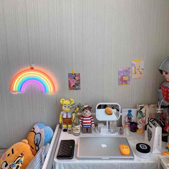 Bright white-toned single household home office desk area featuring rainbow neon lighting and character figurines in a simple room