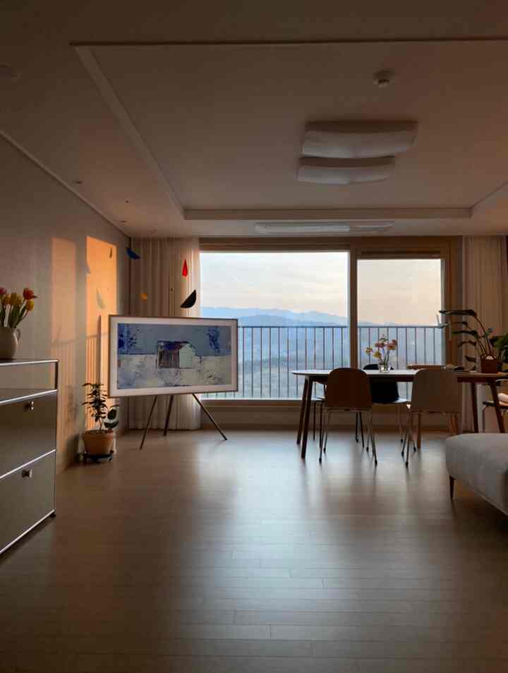 Natural modern living and dining room with warm brown wood flooring, white curtains, and large window showcasing a mountain view