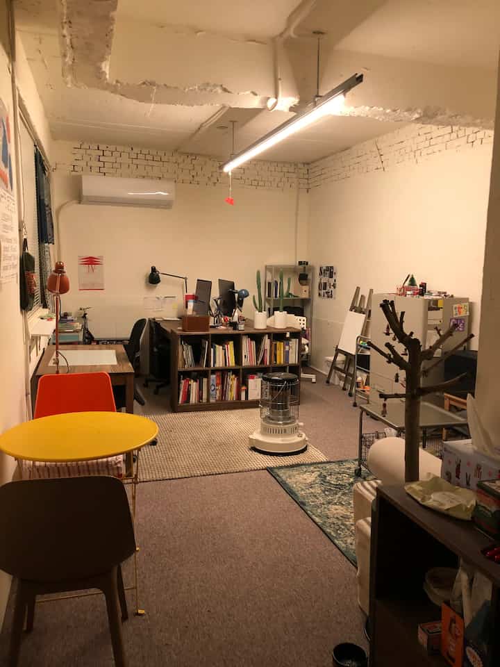 White and brown toned design studio featuring desks and bookshelves centrally arranged with a cozy, creative atmosphere