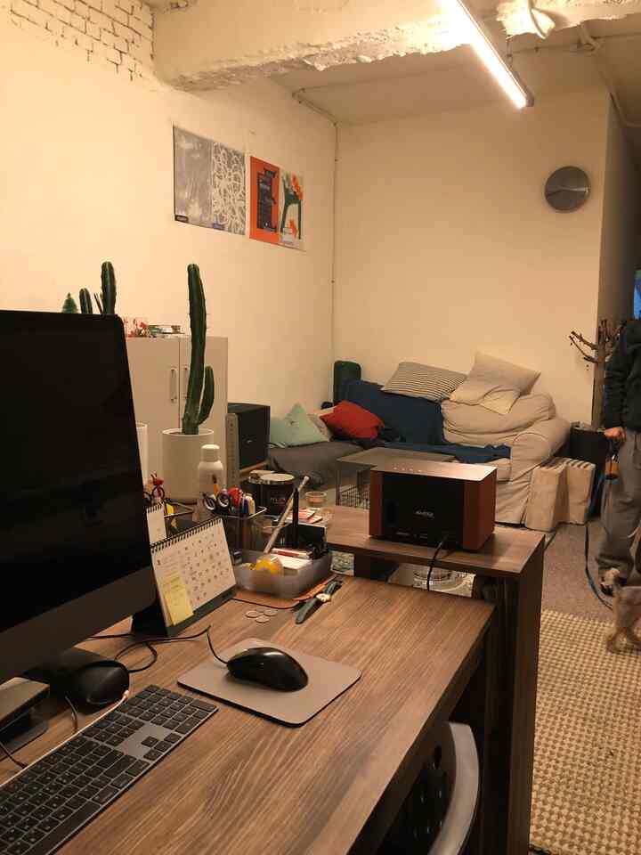 Beige walls and brown wood-tone desk in a home office and relaxation space featuring a sofa and small dog, creating a cozy working area