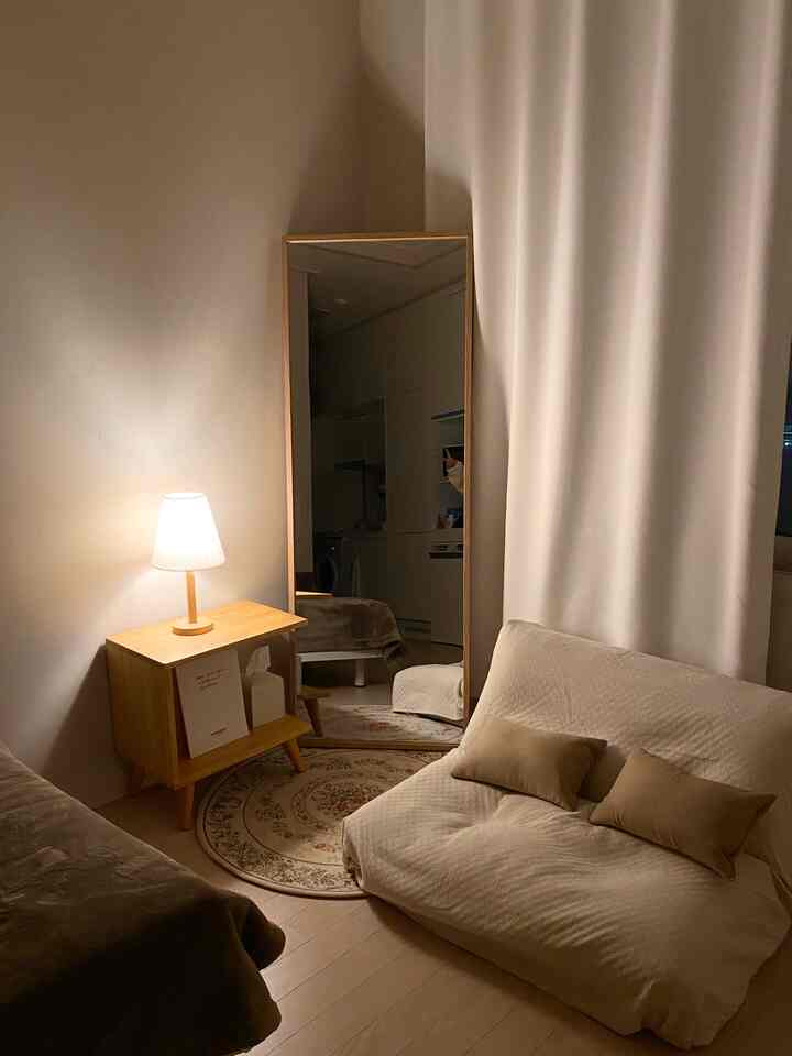 柔らかなベージュと木目調が調和する居心地の良いリビング、ソファベッドと木製サイドテーブルが配置されたミニマルな空間