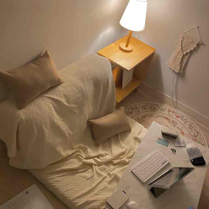 ベージュと木目調の調和が取れたコンパクトなリビング、ソファベッドとサイドテーブル、柔らかな照明が居心地の良い雰囲気を演出しているインテリア