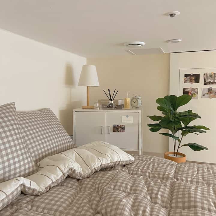 Beige and white toned bedroom featuring checked bedding and white dresser with cozy ambient lighting