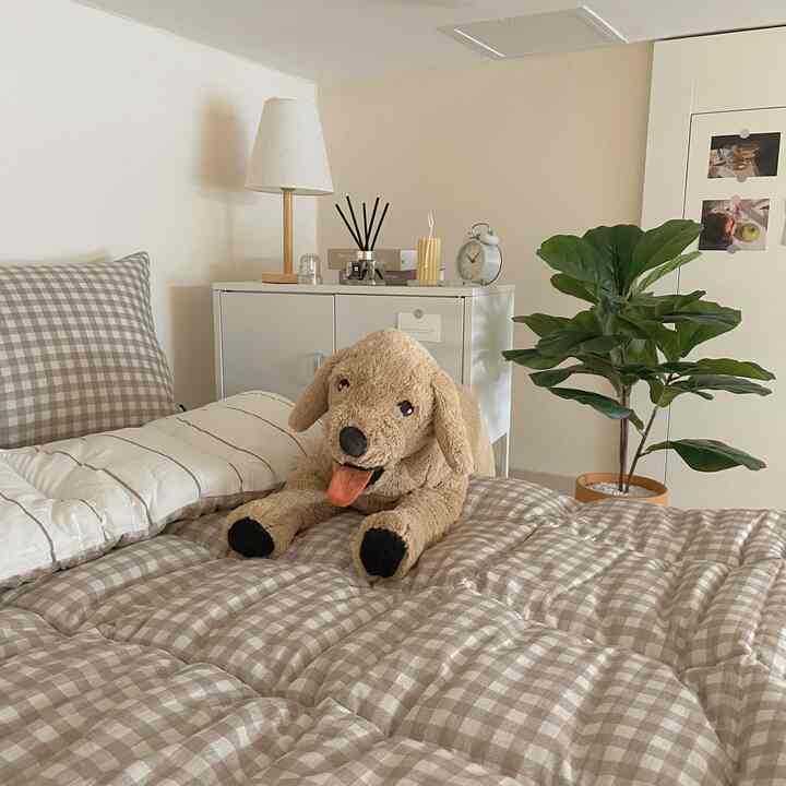 A cozy bedroom in ivory and brown tones with checkered bedding and a plush dog on the bed
