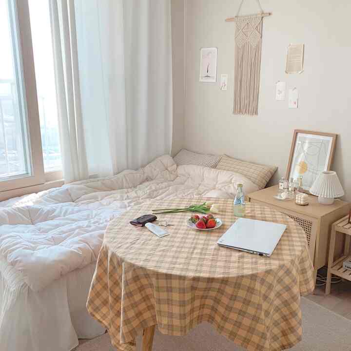 Cozy studio-bedroom in warm beige and white tones featuring a round table and macrame wall hanging