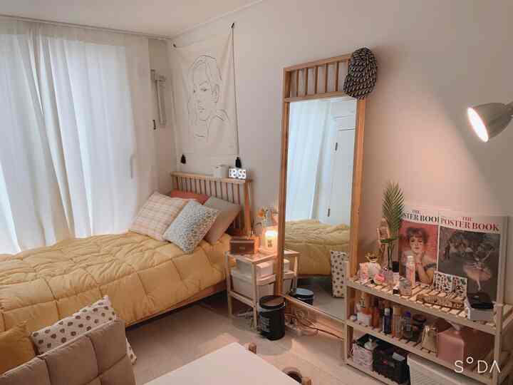 Natural tone single household bedroom featuring yellow bed, wooden mirror, and organized storage for a cozy atmosphere