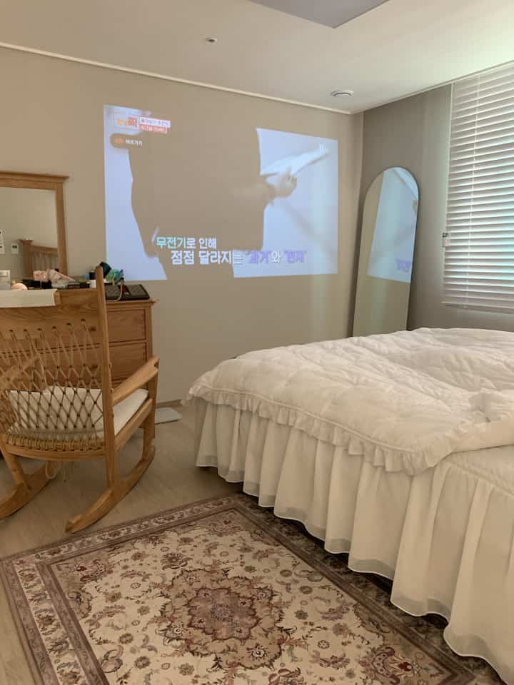 White and wood tone bedroom featuring an arched full-length mirror and a wall-projected screen, creating a warm cozy atmosphere