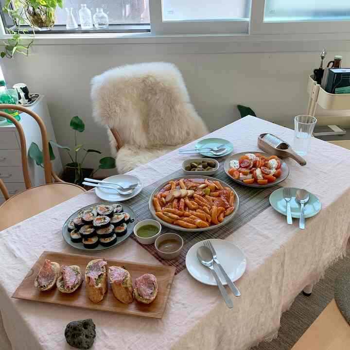 ベージュトーンのキッチンダイニング、ナチュラルな木製椅子とテーブルクロスに様々な料理が並ぶホームパーティーの雰囲気のあるインテリア