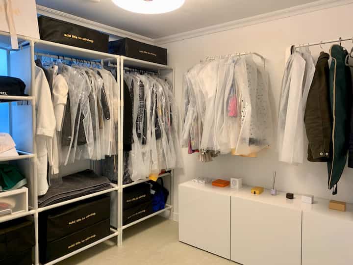 White and natural color walk-in closet featuring organized clothes hanger racks and storage bins in a neat setting
