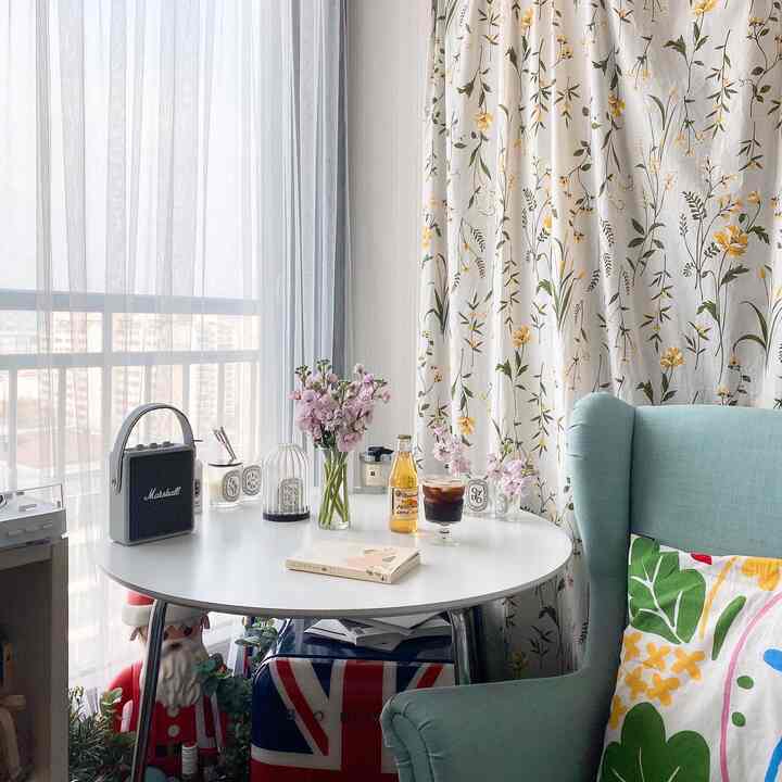White and yellow toned dining room featuring round table, floral curtains, and cushion on armchair with cozy atmosphere