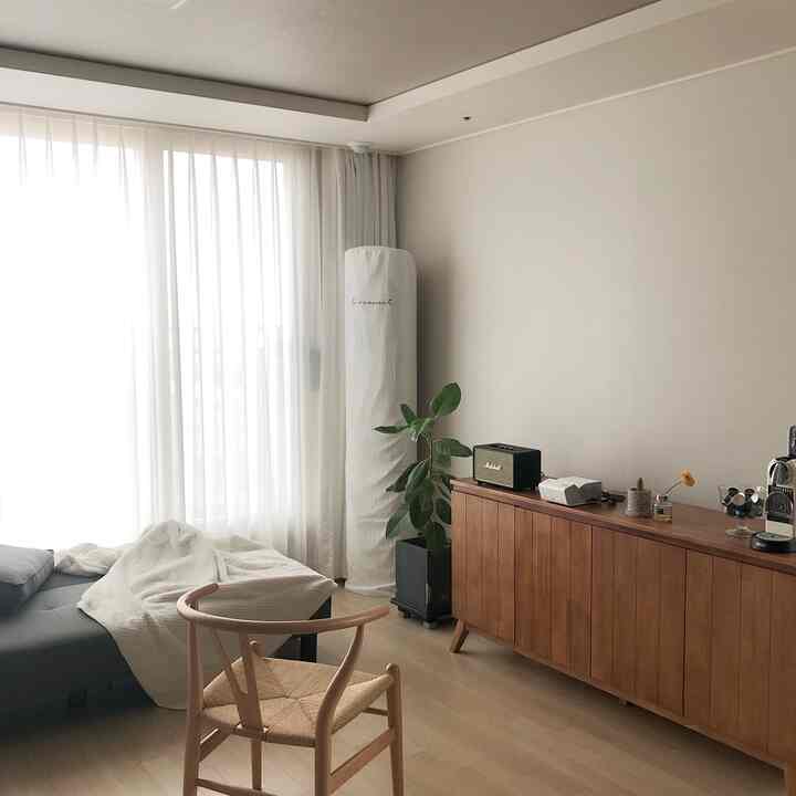 Natural wood tones and white curtains define the living room featuring a wooden chair and sideboard creating a cozy atmosphere