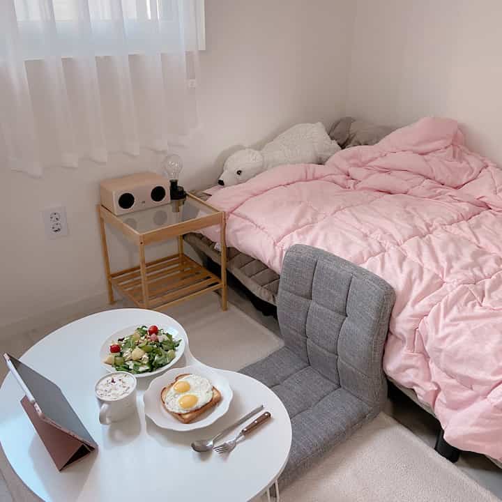 White and pink toned bedroom featuring nightstand and rug in a cozy single household studio apartment