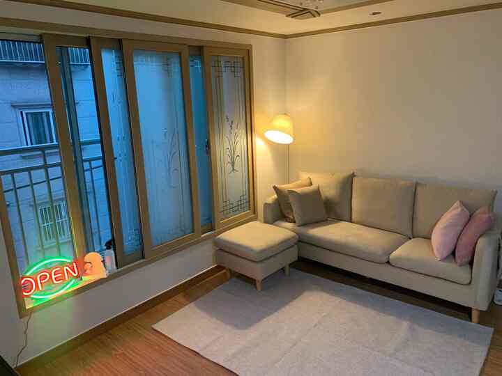 Beige and wood-toned living room with a three-seat sofa, stool, and floor lamp creating a warm atmosphere