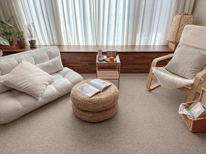 Natural living room with beige and brown wood tones featuring a sofa bed, armchair, and rattan stool creating a cozy atmosphere