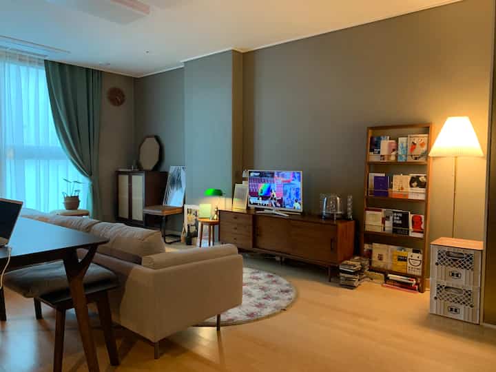Cozy studio living room with warm natural tones, featuring wooden furniture, beige sofa, and floor lamp