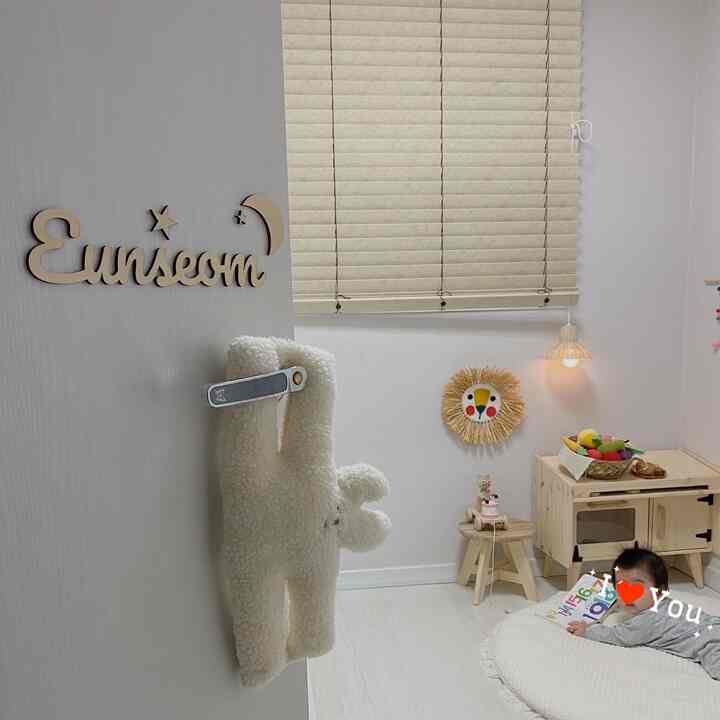 Ivory and beige toned baby room featuring wood blinds, wooden toy storage cabinet, and a baby lying on a cushioned mat with a natural atmosphere