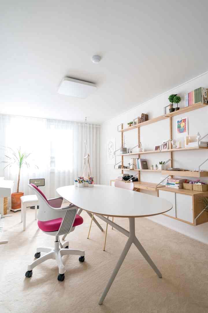 Bright white and beige toned home office space featuring a large white desk and pink office chair centrally placed in a tidy work area