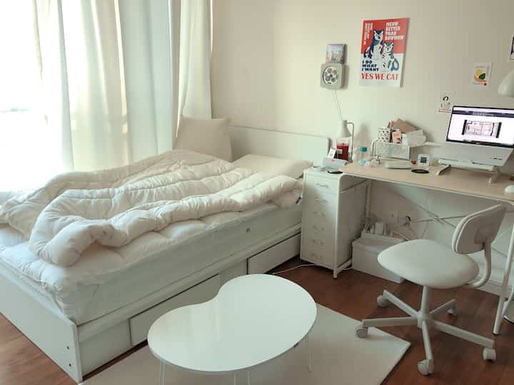 Bright white-toned bedroom featuring neat bed and desk with cat poster, creating a cozy atmosphere