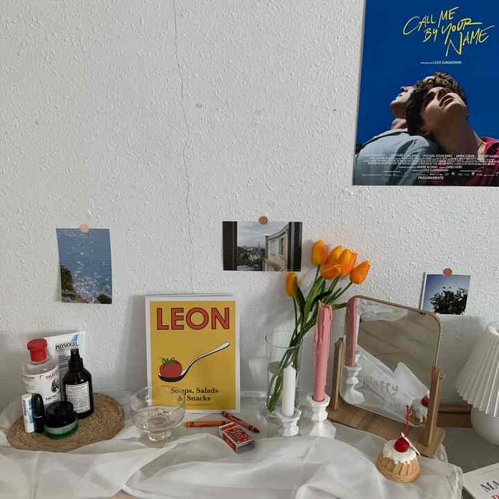 Aesthetic space with white wall and wooden vanity displaying a yellow poster, orange tulips in a glass vase, and pink candles