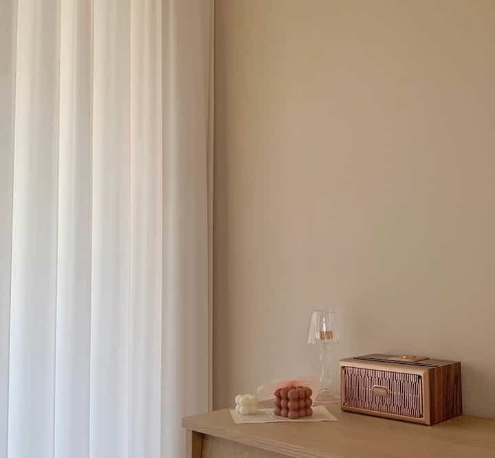 A cozy master bedroom in white and brown tones featuring chiffon curtains, wooden cabinetry, candles and a candle holder