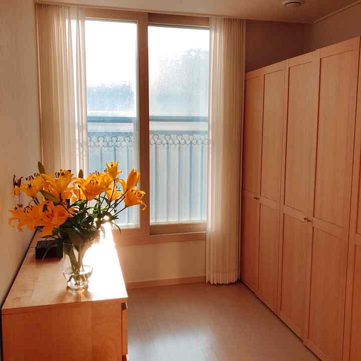 Bright west-facing room with white walls and natural wood tones, featuring yellow flowers on a dresser and large storage cabinet creating a cozy atmosphere