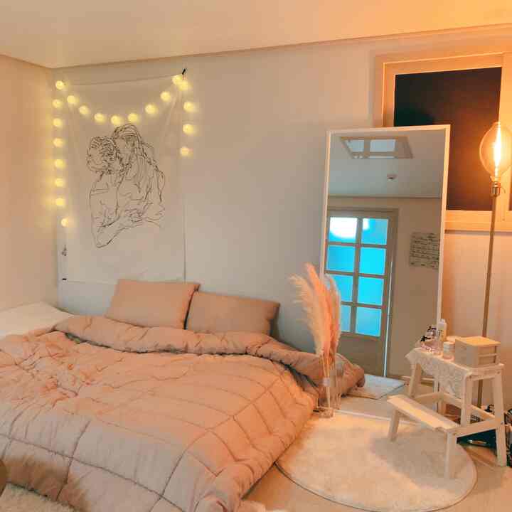 Warm beige and white toned studio bedroom featuring a bed, full-length mirror, and soft lighting creating a cozy atmosphere