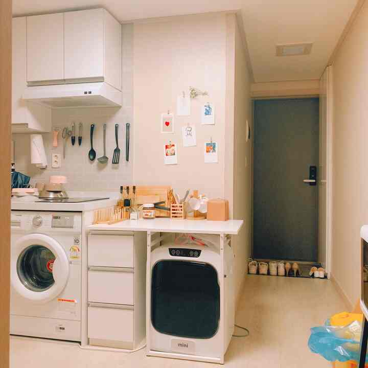 White and gray toned studio apartment kitchen featuring a mini dryer and auxiliary table with efficient storage