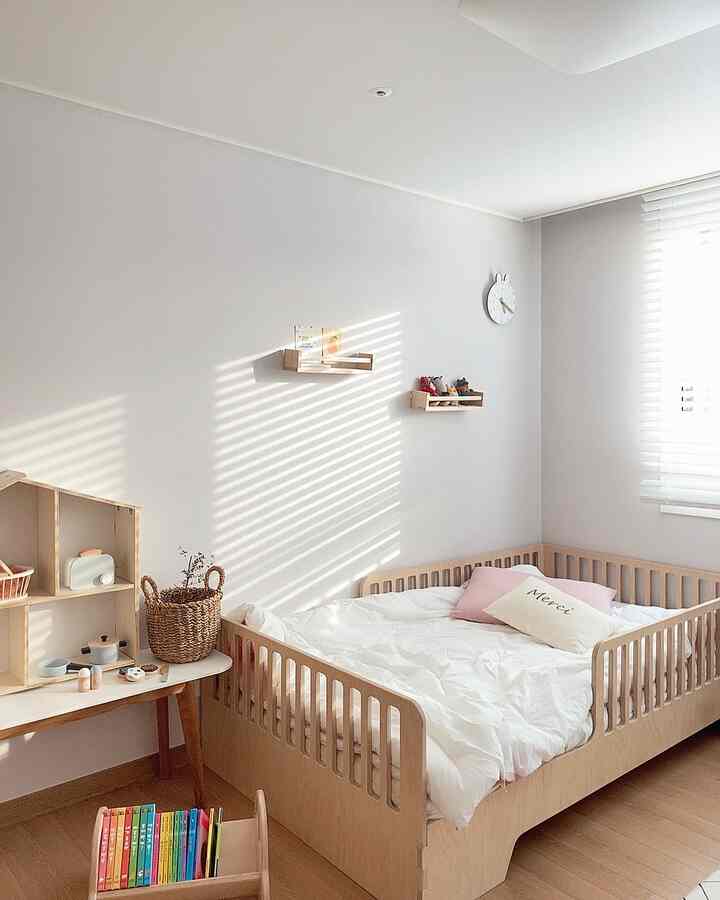 明るい白い壁と木目調のベビーベッド、本棚が配置されたナチュラルで温かみのある子供部屋