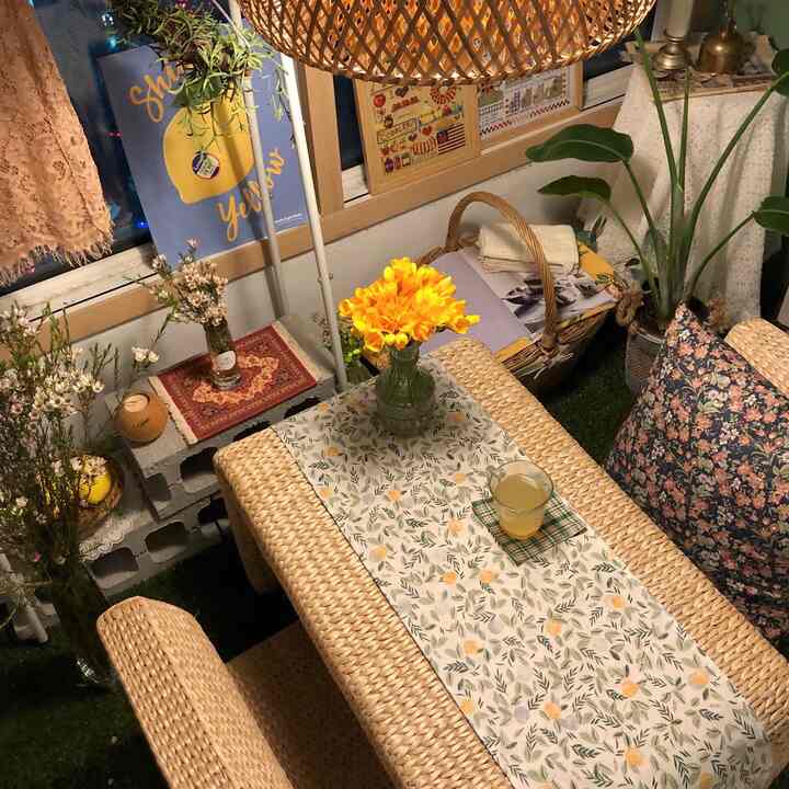 ナチュラルな色調のベランダ、籐製のテーブルと椅子が配置され、黄色い花と様々な植物が調和した雰囲気のあるインテリア