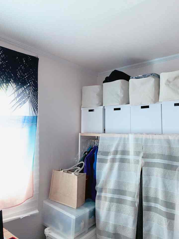 White and natural toned walk-in closet featuring storage boxes and curtains for a neat organized wardrobe