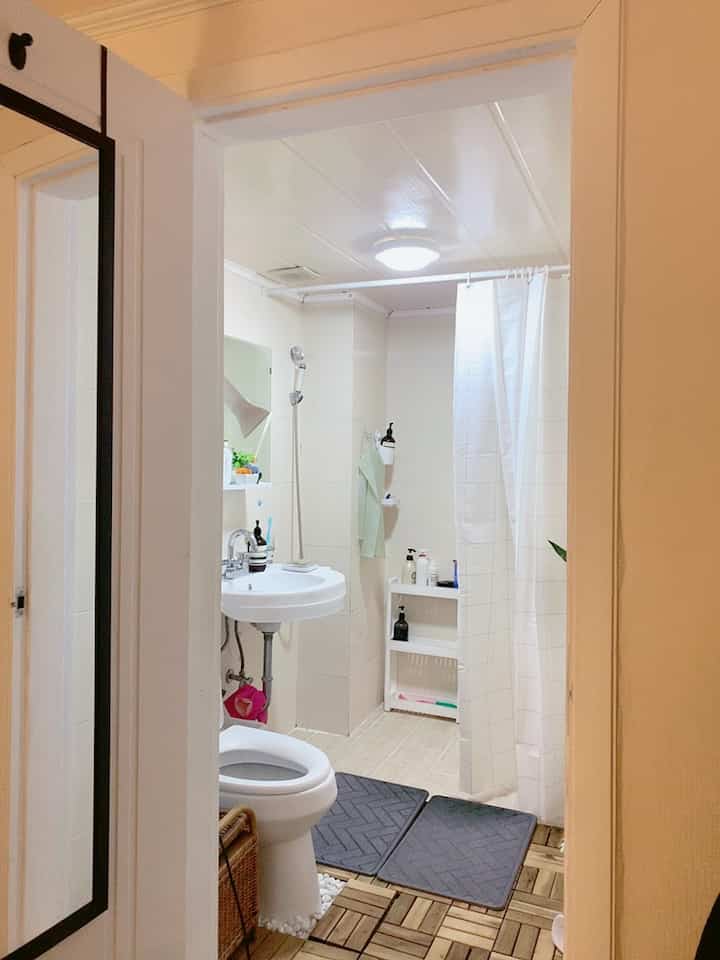 White and wood tone restroom featuring a sink, toilet, shower curtain, and bath mats on deck tile flooring, creating a cozy atmosphere