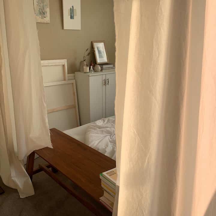 Beige and ivory toned bedroom featuring wooden bench, curtains, and wall art creating a warm natural atmosphere