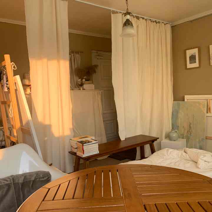 Cozy studio apartment with beige walls, natural wood dining table, and white curtains