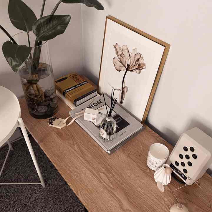 Warm natural bedroom space featuring wood-tone table with plant, picture frame, diffuser, and candle on top