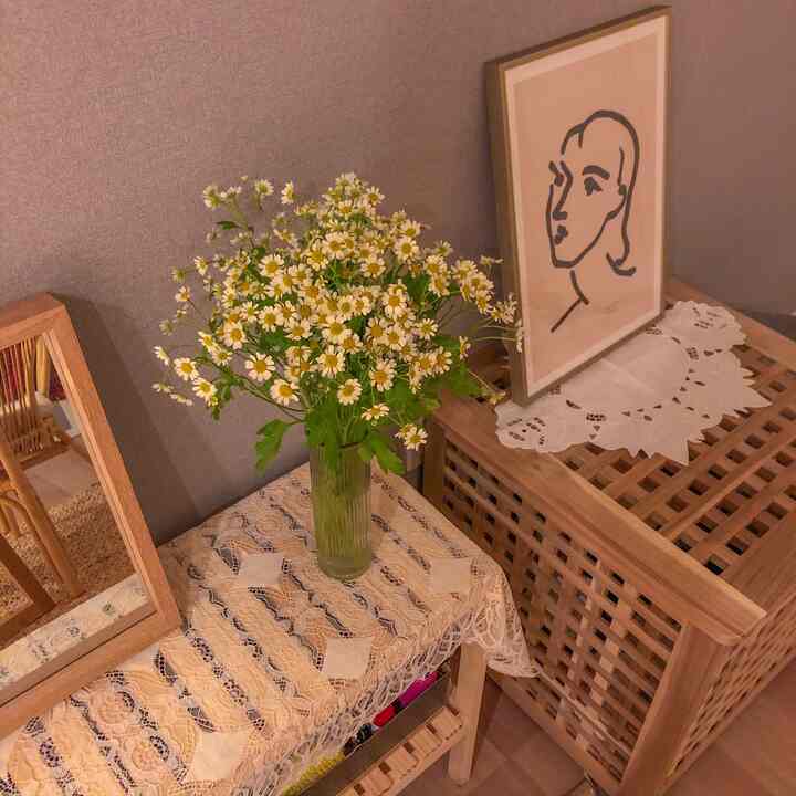 Cozy natural-toned living corner with gray wallpaper backdrop, wooden storage cabinet, vase with flowers, and framed art