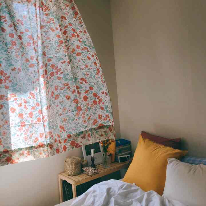 White and yellow toned studio bedroom featuring floral curtain and natural wood shelf creating cozy atmosphere