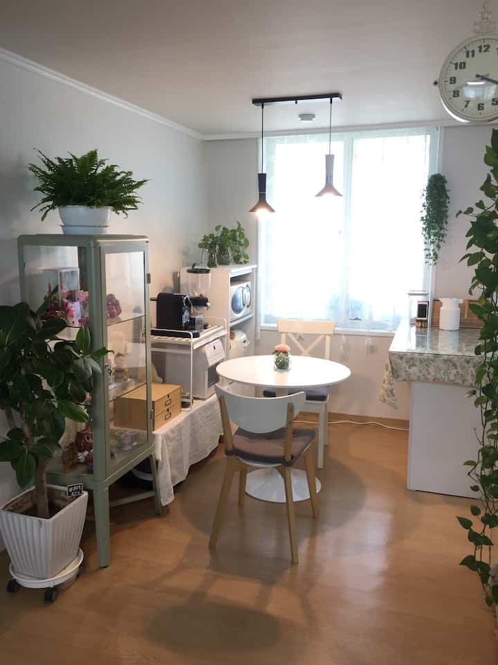 温かみのあるブラウンと清潔感のあるホワイトのキッチン、丸テーブルと植物が配置された雰囲気のあるおうちカフェ空間