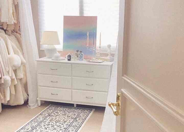 白とベージュの色調のウォークインクローゼットで、白いチェストと照明が置かれた雰囲気のある空間