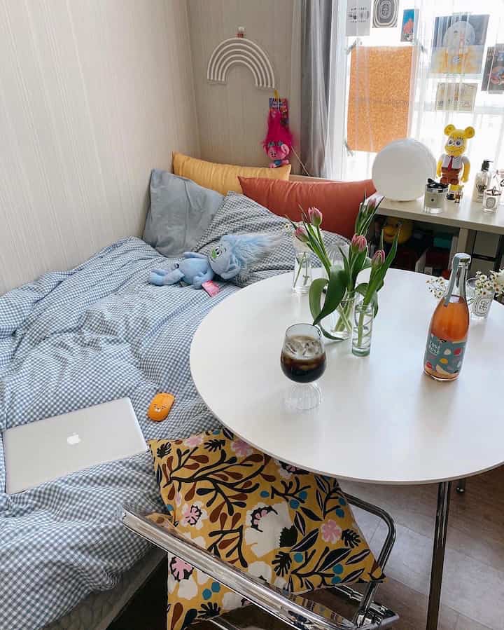 White and blue toned studio bedroom featuring check duvet, cushions, tulips, and drinks on table in cozy setting