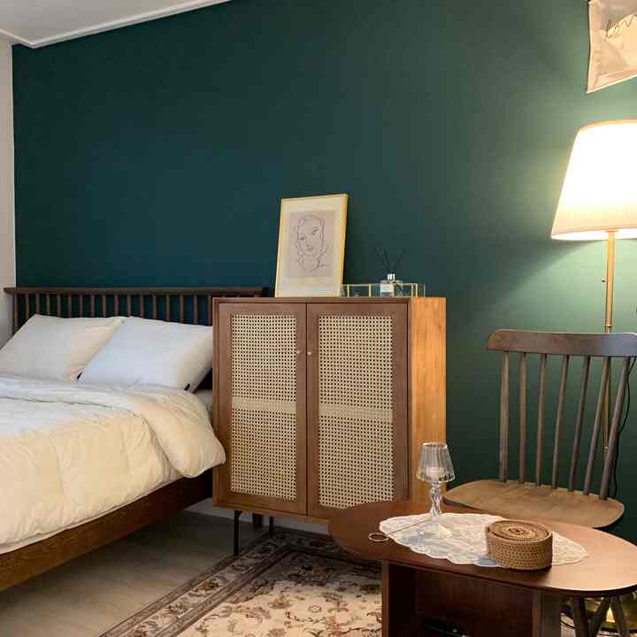 深いグリーンの壁と木目調の家具が配置されたナチュラルな寝室のインテリア