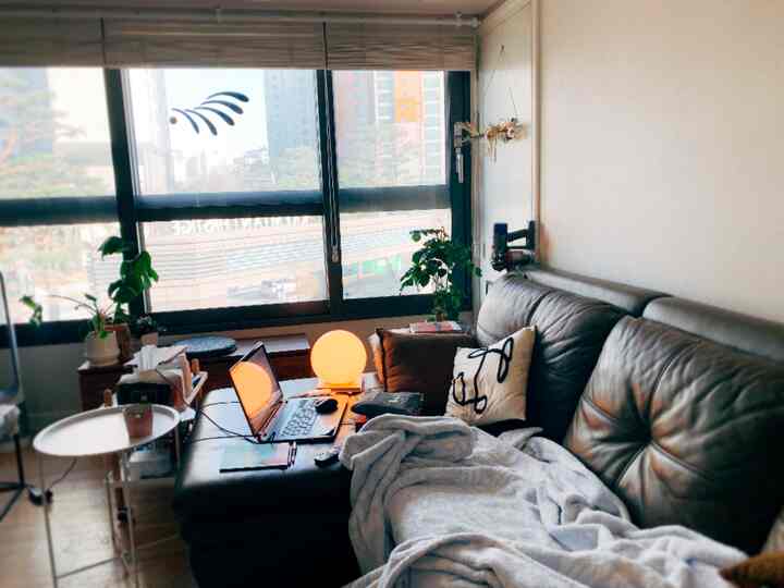 温かみのあるトーンの小さなリビング、革製の大きなソファとサイドテーブル、丸いテーブルランプが配置された落ち着いた空間