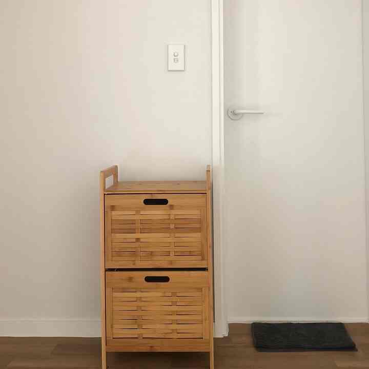 A simple modern bathroom featuring white walls, brown wood-tone flooring, and a bamboo 2-tier storage cabinet beside the door