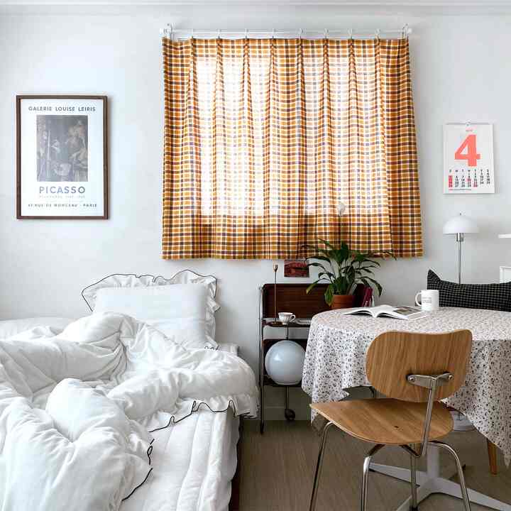 White and yellow toned bedroom featuring white bedding, yellow checked curtain, round table, and plant in a cozy atmosphere